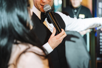 Man in formal wear gestures with microphone to musician, adding fun to the event - obrazy, fototapety, plakaty