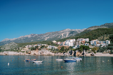 Fishing boats are moored in the sea near colorful hotels on a rocky slope. Przno, Montenegro
