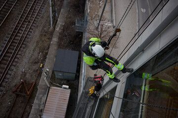 High angle view of rope access worker hanging on glass building by railroad tracks