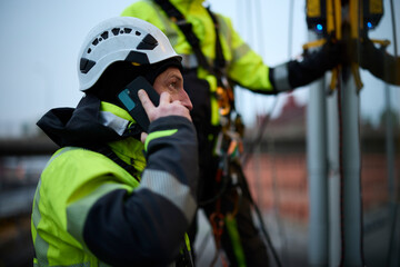 Male rope access worker talking on phone outside window of building