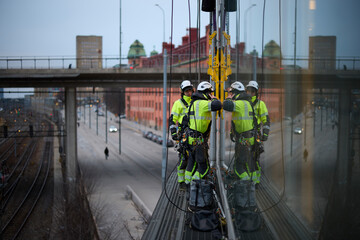 Rope access workers standing on structure outside window glass of building