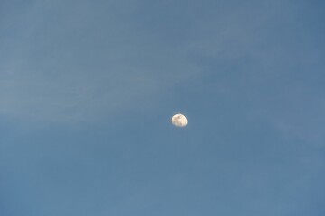 Beautiful shot of the white half-moon in a bright blue sky