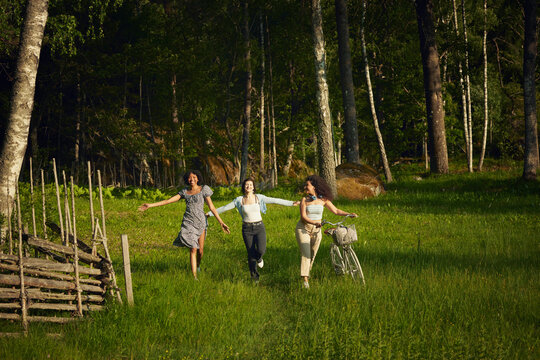 Cheerful friends running together with bicycle in forest
