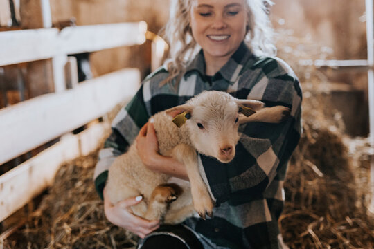 Smiling woman carrying sheep kid in farm