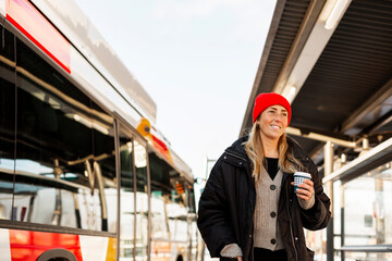Contemplative woman with disposable cup standing at bus stop