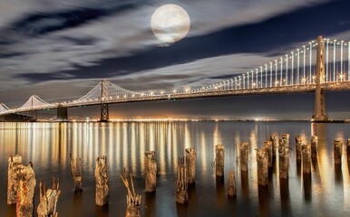 Gorgeous view of the Golden Gate Bridge with a full moon in the cloudy sky on a bright night
