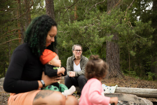 Smiling mature woman looking at young mother with two children in forest