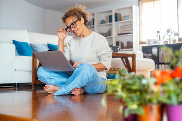One midage lady sitting on the floor comfortable using laptop at home in indoor technology wireless leisure activity alone. Modern female people working on computer. Woman browsing web and writing