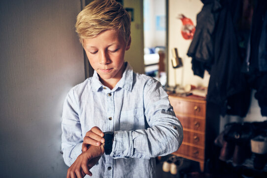 Blond boy checking time on wristwatch at home
