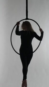 Silhouette of a Caucasian woman dancing on acrobatic aerial hoop over grey background. Gymnastic show performance. Vertical video.