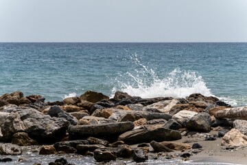 Beautiful foamy waves splashing onto a rocky beach against a blue seascape