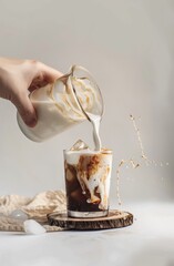 A hand pours milk into glass with coffee