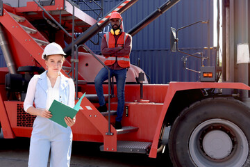 Happy beautiful woman boss with safety helmet holds document folder, stands at logistic shipping cargo containers yard with African engineer worker man and crane at background. People at workplace.