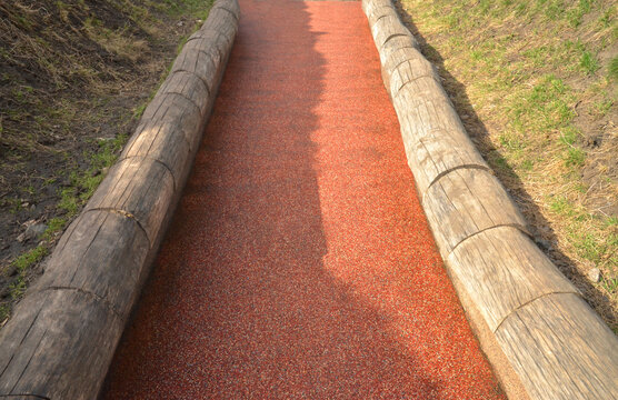 Soft red colored bicycle path (road) framed by wood, closeup