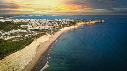 Drone view of the blue ocean with the city and sandy beach at sunset in Porto do mos, Portugal