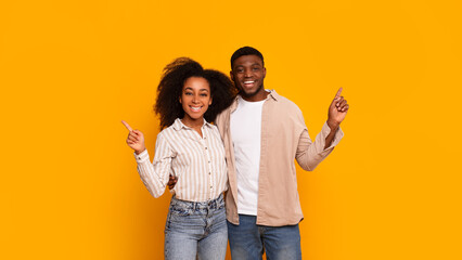 Couple pointing up together on yellow background - obrazy, fototapety, plakaty