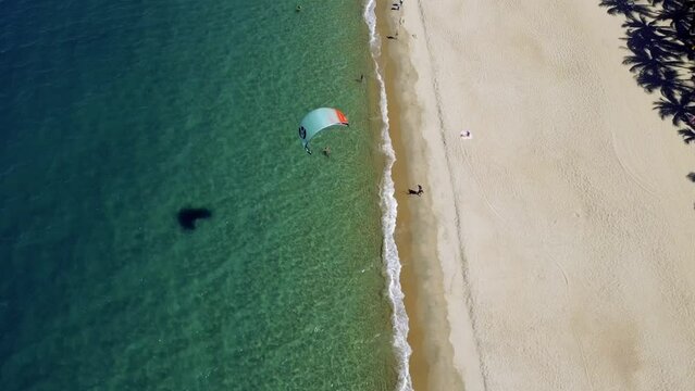 Athlete ride on the board makes a turn. Drone fly around kitesurfer. Drone footage of kiter riding at sunset. The ocean has clear blue water. A kite surfers rides in ocean lagoon.