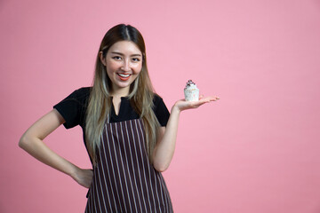 Young asian woman with an apron in celebratory or festive mood holding cupcake, decorated with...