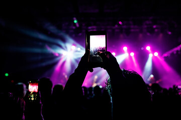 A hand holds a smartphone, recording a lively event illuminated by colorful lights