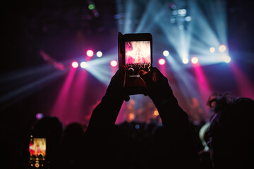 A hand holds a smartphone, recording a lively event illuminated by colorful lights
