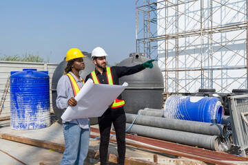 Two construction worker standing together in front of a large building site with helmet and safety...