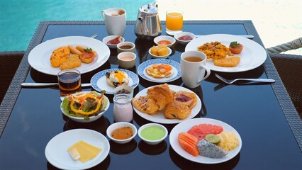 Luxurious breakfast spread at resort with variety of dishes including fruits, pastries, drinks, and hot meals. Exotic dining experience with view.