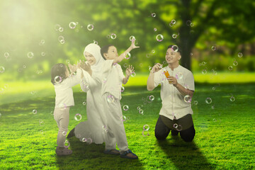 Young parents playing soap bubbles with their children at park