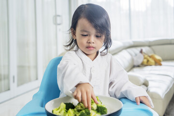 Asian Child little girl eats vegetable broccoli using hand