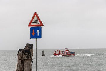 Traffic sign priority in oncoming traffic and attention roadside on the coast of the Venice Lagoon. Passenger ferry in the background