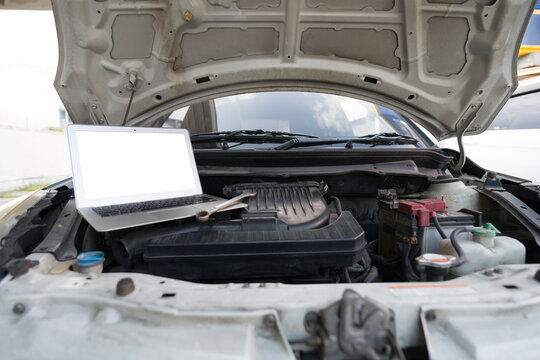 A blank screen laptop computer and wrench tool placing inside car's hood on car engine.