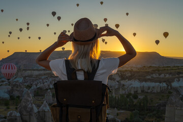 Female tourist in a hat with a backpack stands alone at the top and admires the flight of balloons...