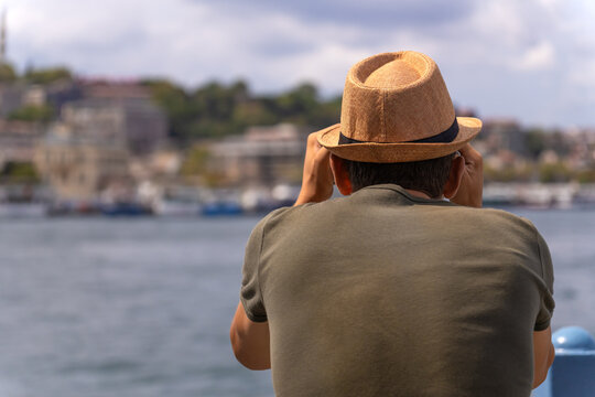 Man tourist in a hat looks through binoculars on the Galata Bridge in Istanbul, Turkey, photo from the back, copy space. Concept of travel and tourism. Observation deck for tourists