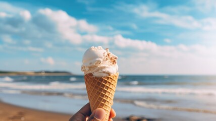 A hand holding a melting ice cream cone against a sunny beach background.