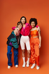Obraz premium A diverse group of women standing together, exuding beauty and unity against an orange studio backdrop.