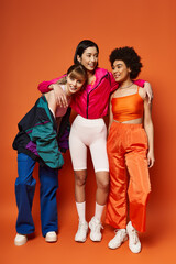 Fototapeta premium A group of multicultural women, including Caucasian, Asian, and African American, stand together harmoniously against an orange background.