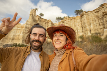 A man and a woman are posing for a picture in front of a mountain. The man is wearing a brown jacket and the woman is wearing a brown hat. They are both smiling