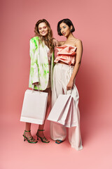 Two multicultural women standing side by side, holding shopping bags on a vibrant pink background.
