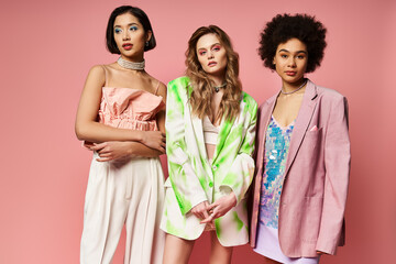 Three diverse women stand gracefully together against a pink background, showcasing beauty in their unity.