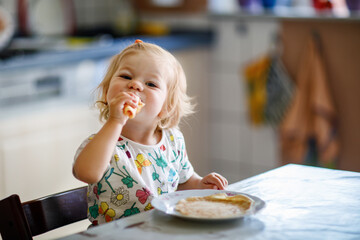 Happy little toddler girl eating delicious pancakes sitting in the kitchen. Cute child tasting different food