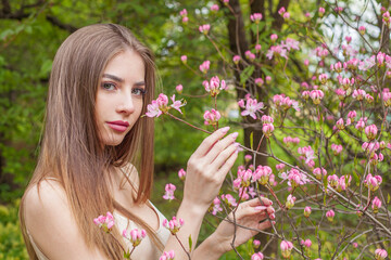 Glamorous young woman with natural makeup and healthy long brown hair in blossom park outdoors. Natural female beauty portrait