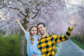 Father's Day Cute little blue-eyed girl with her smiling dad in blossoming sakura garden. Warm...