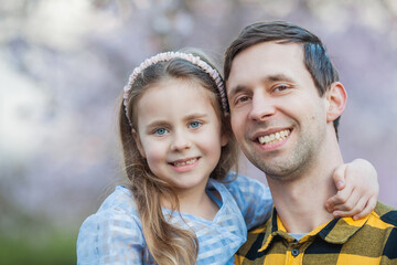Father's Day Cute little blue-eyed girl with her smiling dad in blossoming sakura garden. Warm bright spring.