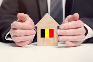 Businessman hand holding wooden home model with Belgium flag. insurance and property concepts
