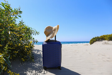 Single suitcase and a straw hat by the entrance to the beautiful tropical beach. Symbolic vacation objects. Close up, copy space, background.