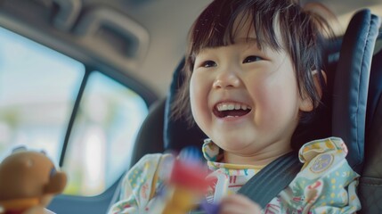 Young child in car seat smiling broadly holding a toy with joyous expression looking towards the camera.