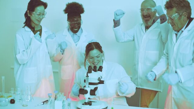 group of jubilant university scientists celebrates a successful experiment in the lab, with one researcher looking through a microscope