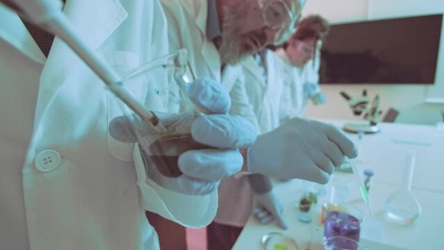scientist carefully pours a solution from a beaker in a bright laboratory, with colleagues working in the background