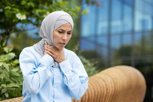Worried woman in hijab feeling irritation in throat and experiencing symptoms of flu virus while walking down street. Ill female touching sore spot on body and thinking about prescript treatment.
