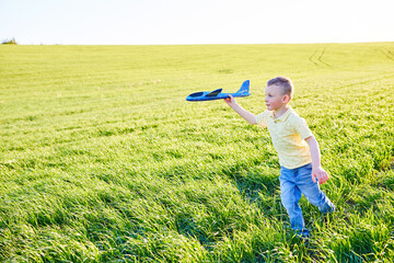 Boy runs with toy airplane in summer through field. Happy child running and playing with toy...