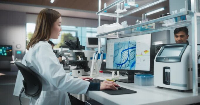 Smart Japanese Female Scientist Working on a Desktop Computer with Advanced DNA Diagnostic Software on Screen. Diverse People at Work in a Modern Genetic Engineering Research Laboratory